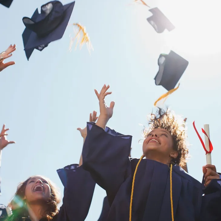 Graduates celebrating by tossing their caps in the air under a clear sky.