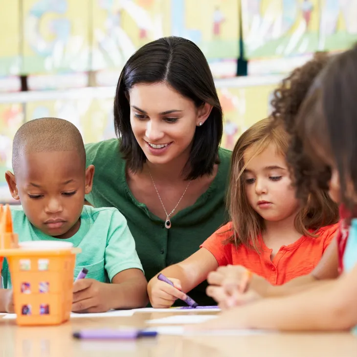 A teacher is engaging with young students during an activity at a classroom table.